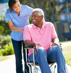 Carer Pushing Senior Man In Wheelchair