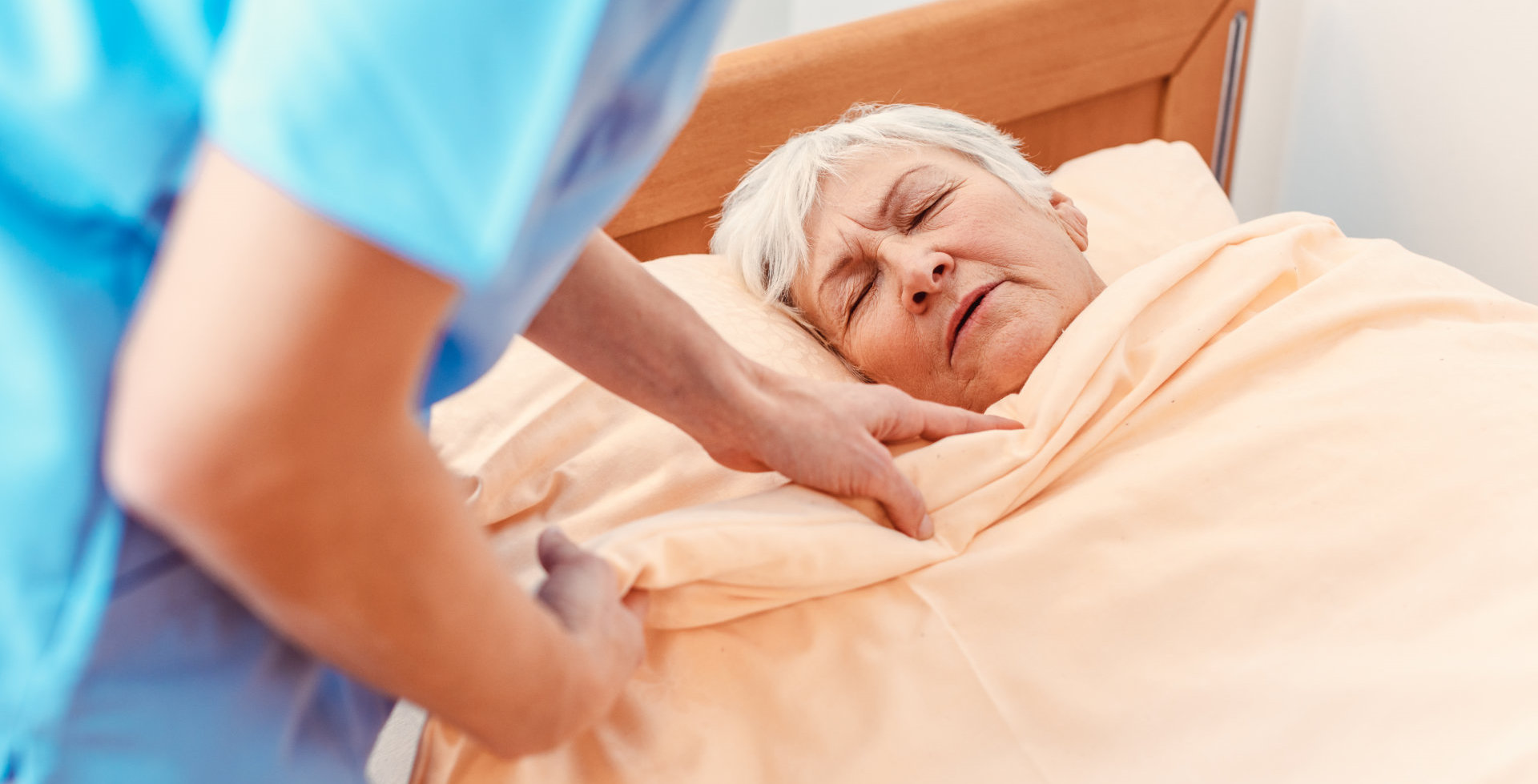 Caregiver pulling blanket over sleeping senior